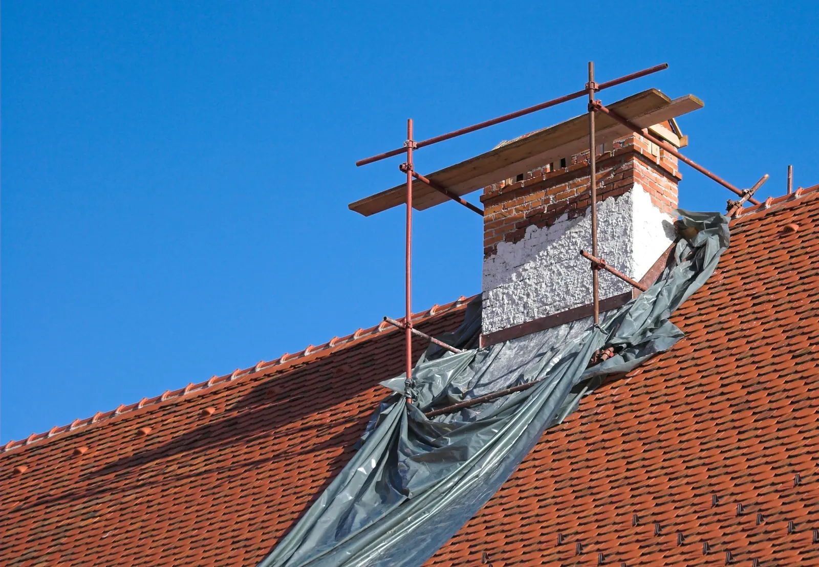 Chimney under scaffolding on a red tile roof