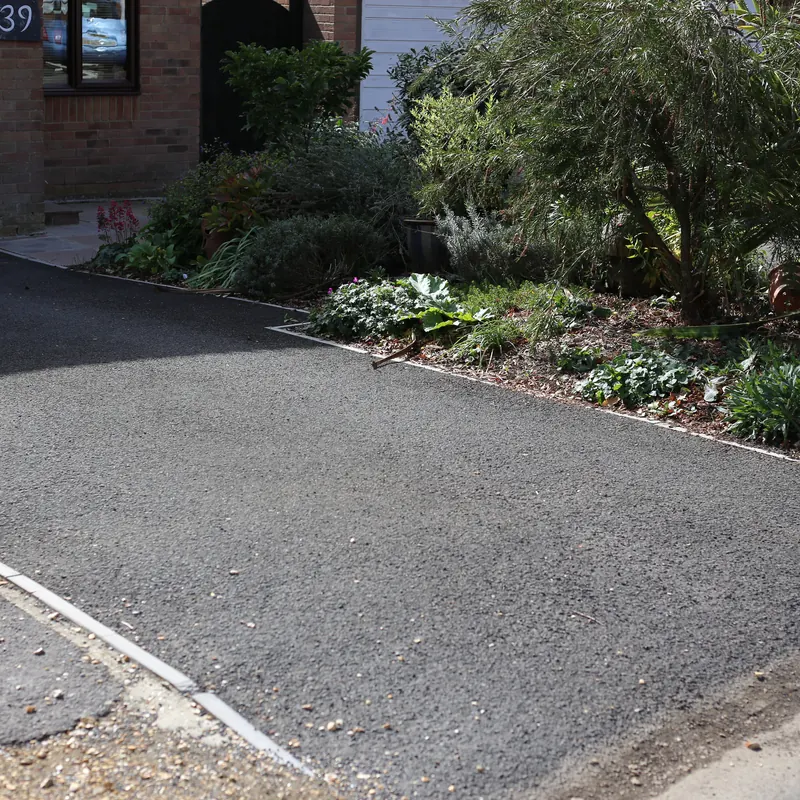 New tarmac driveway with edging beside a planted border